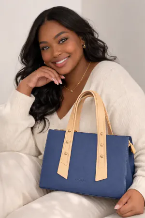 Woman holding Emlonc Vespara tote bag in blue vegan leather with beige handles in a relaxed indoor setting